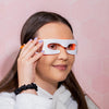 Eine langhaarige Frau trägt die Brille mit rotem LED-Licht vor einem rosa sechseckigen Hintergrund und hält sie mit einer Hand.