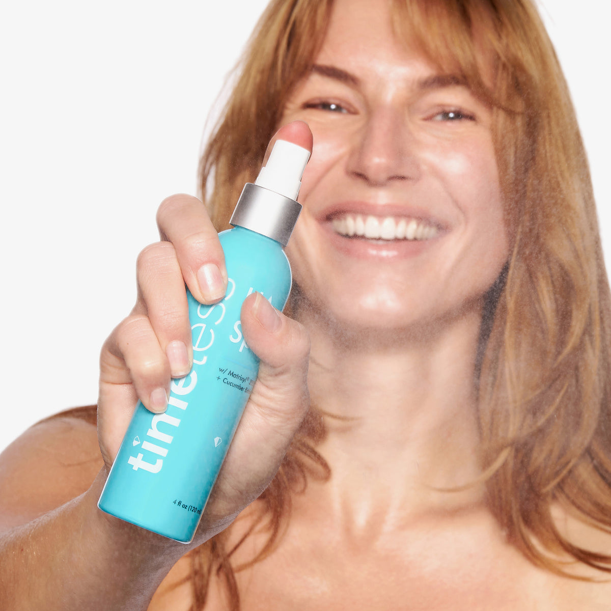 Eine Frau sprüht das Timeless HA Spray mit Gurkenextrakt aus einer türkisfarbenen 120-ml-Sprühflasche. Ein feiner Sprühnebel ist sichtbar.