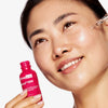 Eine Frau lächelt, während sie das Matrixyl 3000 Serum mit einer Pipette auf ihre Wange aufträgt und dabei die pinke Flasche hält.