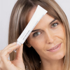 Eine Frau hält eine Tube Adult Acne Treatment an ihre Stirn und lächelt sanft.