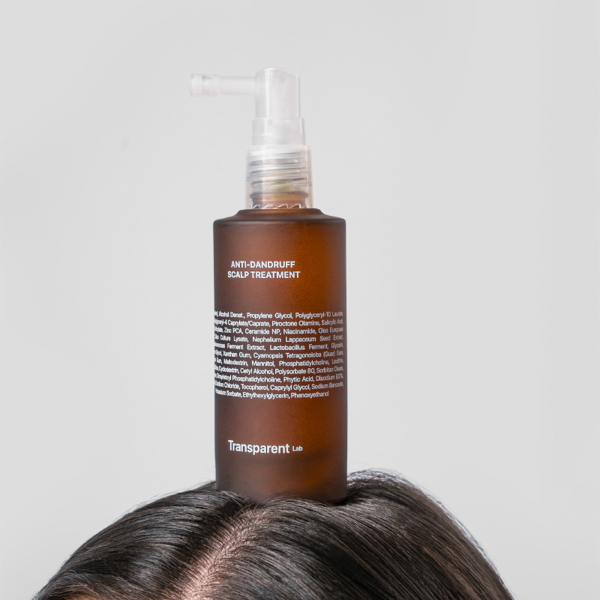 Eine braune Flasche mit der Aufschrift „Anti-Dandruff Scalp Treatment“ steht auf dem Kopf einer Person.
