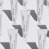 Reihen von Tuben des De-Bloat Soothing Eye Serum mit schwarzem Text auf weißem Hintergrund, der weiche Schatten wirft.