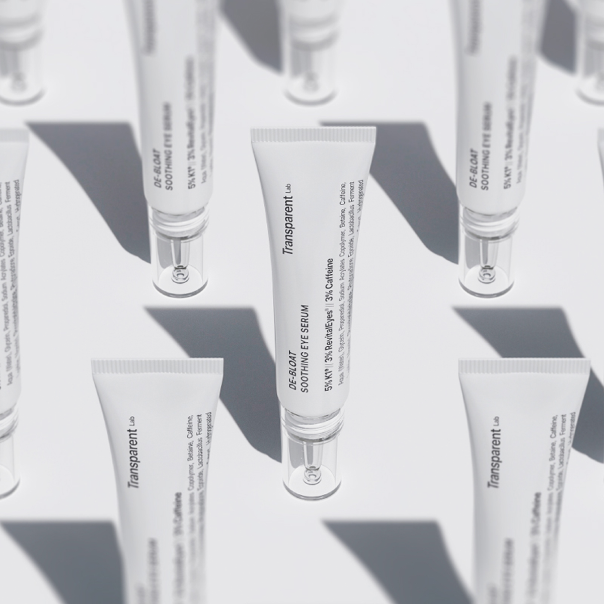 Reihen von Tuben des De-Bloat Soothing Eye Serum mit schwarzem Text auf weißem Hintergrund, der weiche Schatten wirft.