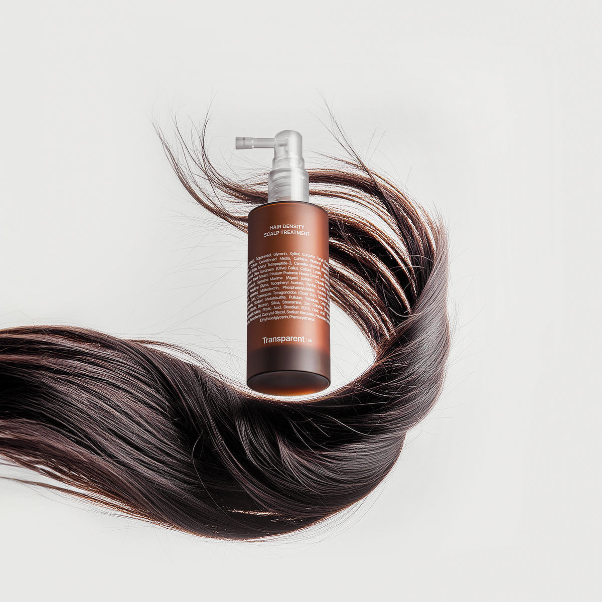 Das Hair Density Scalp Treatment in einer braunen Pumpflasche ist umgeben von wallenden dunklen Haarsträhnen vor hellem Hintergrund.
