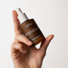 Eine Hand hält eine braune Tropfflasche mit der Aufschrift Liposomal DHA Face Tanner von Transparent Lab.
