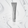 Die Volume Hydrating Lip-Plumping Treatment in einer silbernen Kosmetiktube wird auf einem strukturierten, klaren Flüssigkeitshintergrund mit winzigen Bläschen präsentiert.