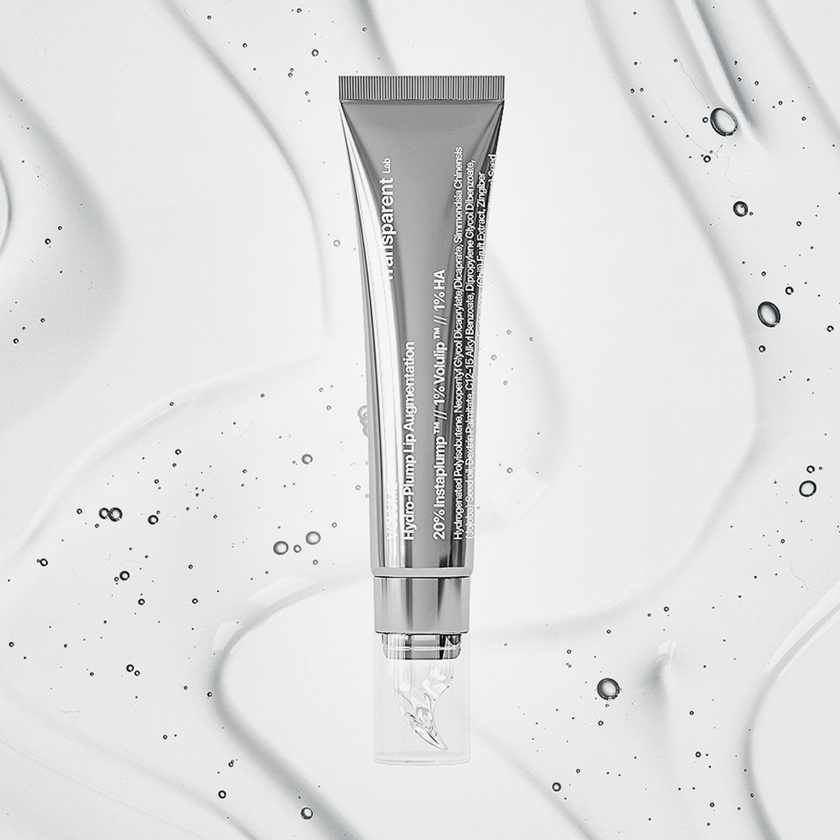 Die Volume Hydrating Lip-Plumping Treatment in einer silbernen Kosmetiktube wird auf einem strukturierten, klaren Flüssigkeitshintergrund mit winzigen Bläschen präsentiert.