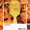 Eine gelbe UNbrush Detangling Hair Brush namens Amber auf einem Hintergrund aus polierten Bernsteinen.