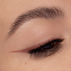 Nahaufnahme des Auges einer Person mit braunem Eyeliner mit Flügeln, der mit Cupid’s Arrow Longwear Stylo gezeichnet wurde, und langen, definierten Wimpern.