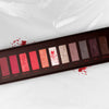 Die „Dexter“-Palette von Lethal Cosmetics: 12 rote, rosa, braune und glitzernde Farbtöne mit gruseligen Namen auf weißem, mit roten Spritzern verziertem Untergrund.