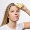 Eine Person hält mit neutralem Gesichtsausdruck eine Flasche Zitcalm Serum an ihre Stirn.