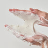 Hände halten und verteilen den weißen, aufgeschäumten Schaum von Heartleaf Quercetinol Pore Deep Cleansing Foam vor einem schlichten, hellen Hintergrund.