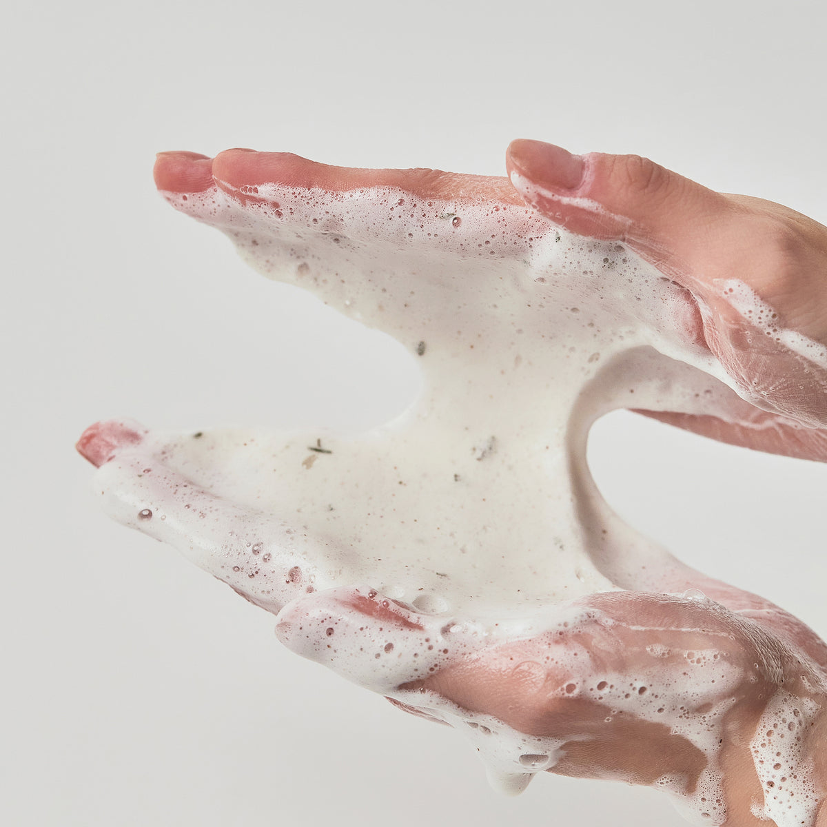 Hände halten und verteilen den weißen, aufgeschäumten Schaum von Heartleaf Quercetinol Pore Deep Cleansing Foam vor einem schlichten, hellen Hintergrund.