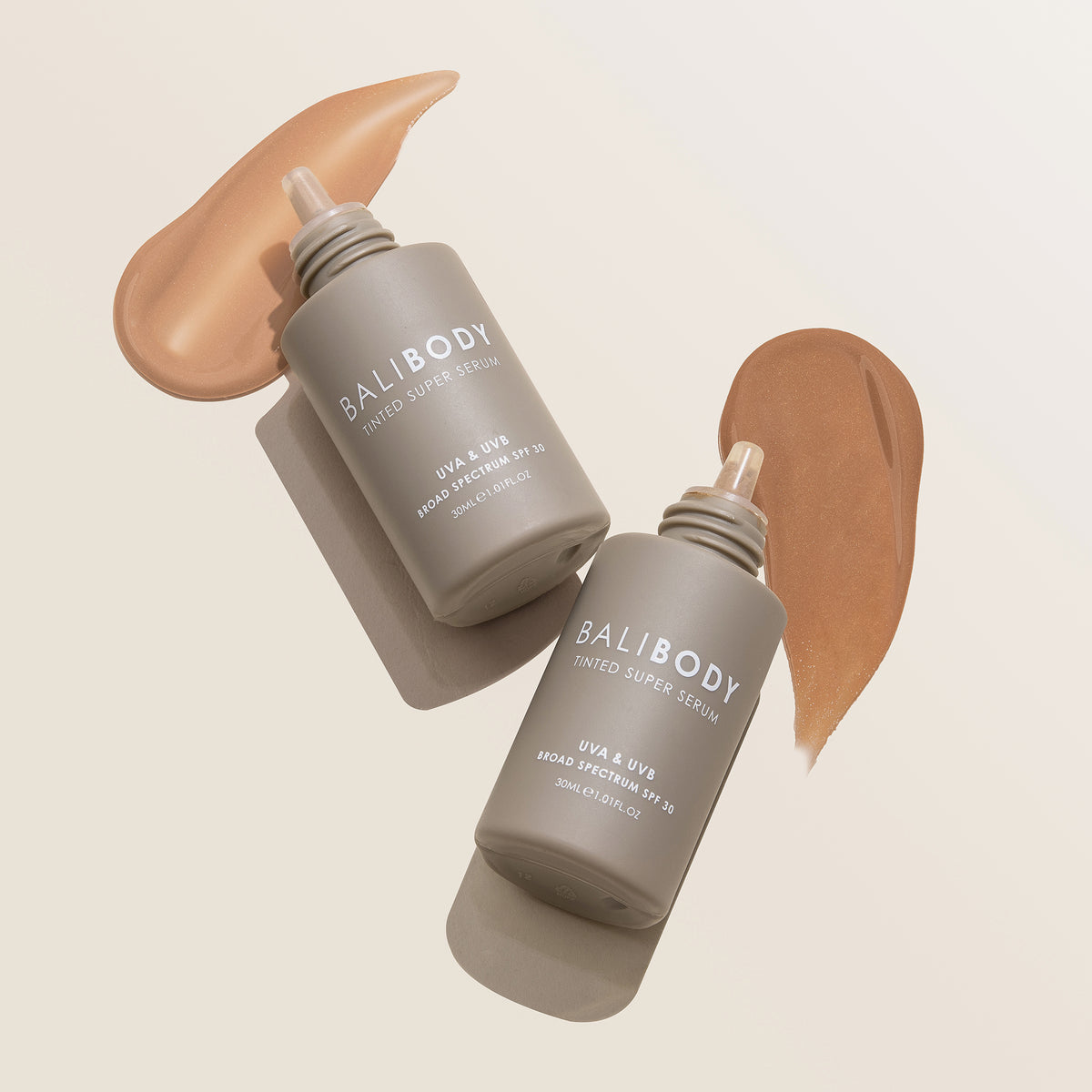 Zwei Tinted Super Serum SPF 30 mit Swatches liegen auf beigem Untergrund