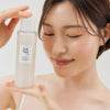 Eine Frau mit dunklem Haar hält die Glow Repleneshing Rice Milk und lächelt.