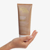 Eine Hand hält eine Tube Gradual Tanning Lotion Tinted Skin Perfector vor einem weißen Hintergrund