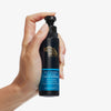 Hand hält eine Flasche Self Tanning Face Mist One Hour Express vor einem weißen Hintergrund