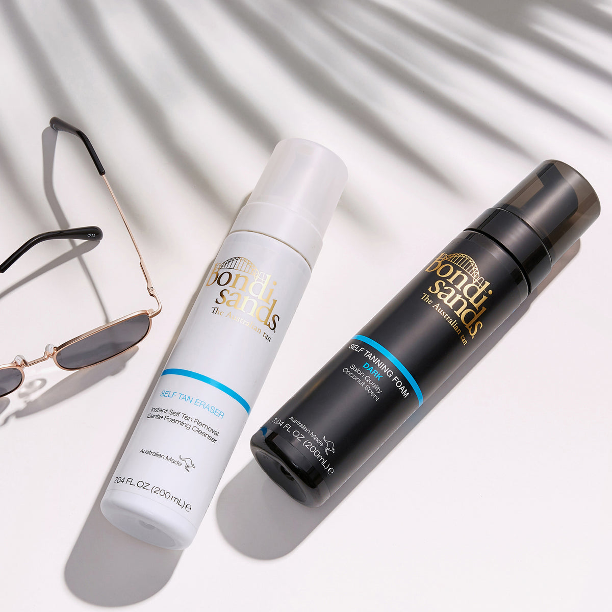 Bondi Sands Self Tanning Foam und Self Tan Eraser liegen auf einer weißen Fläche neben einer Sonnenbrille