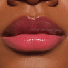 Nahaufnahme glänzender Lippen mit pinkem Lip Oil, das einen intensiven, saftigen Farbglanz auf dunkler Haut zaubert.