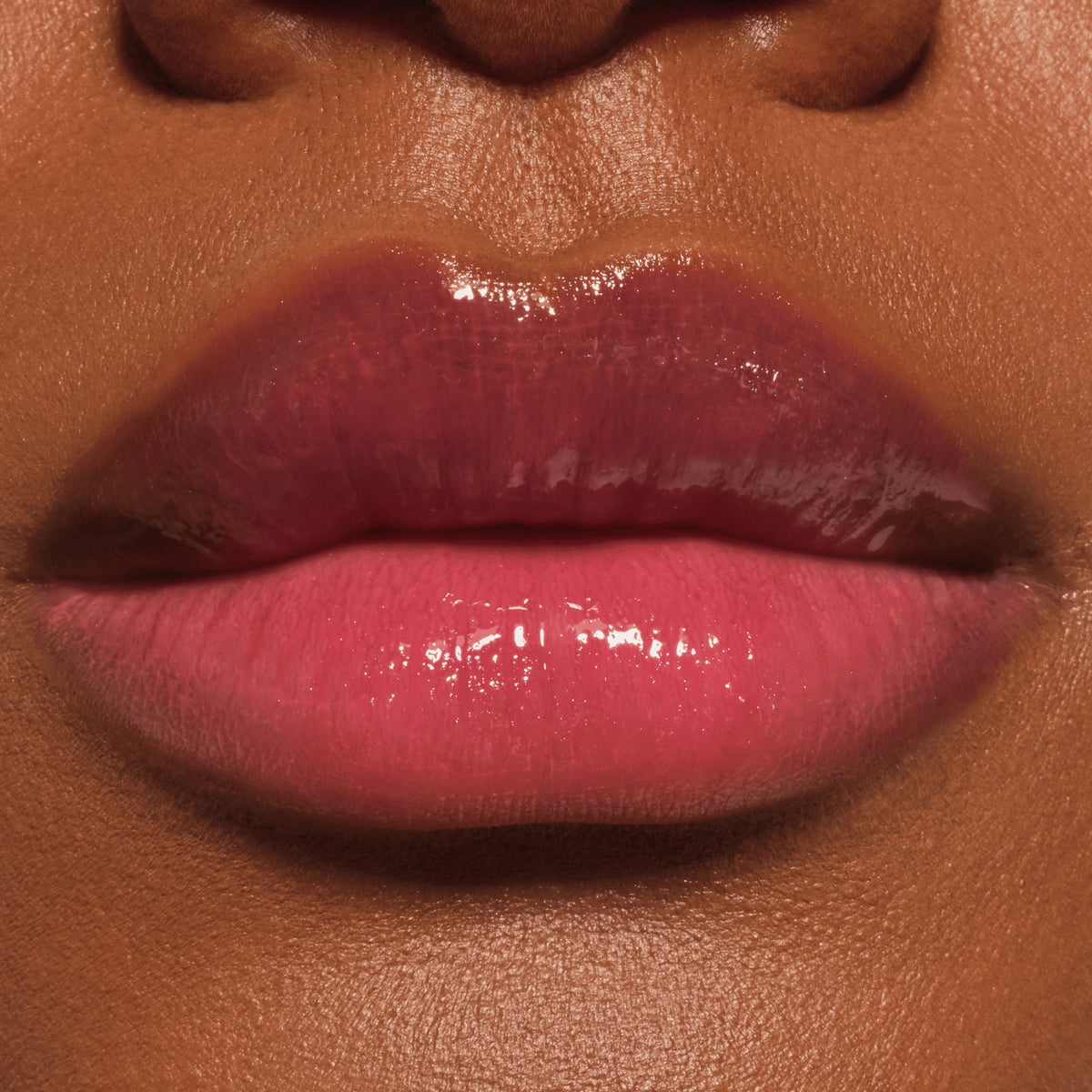Nahaufnahme glänzender Lippen mit pinkem Lip Oil, das einen intensiven, saftigen Farbglanz auf dunkler Haut zaubert.