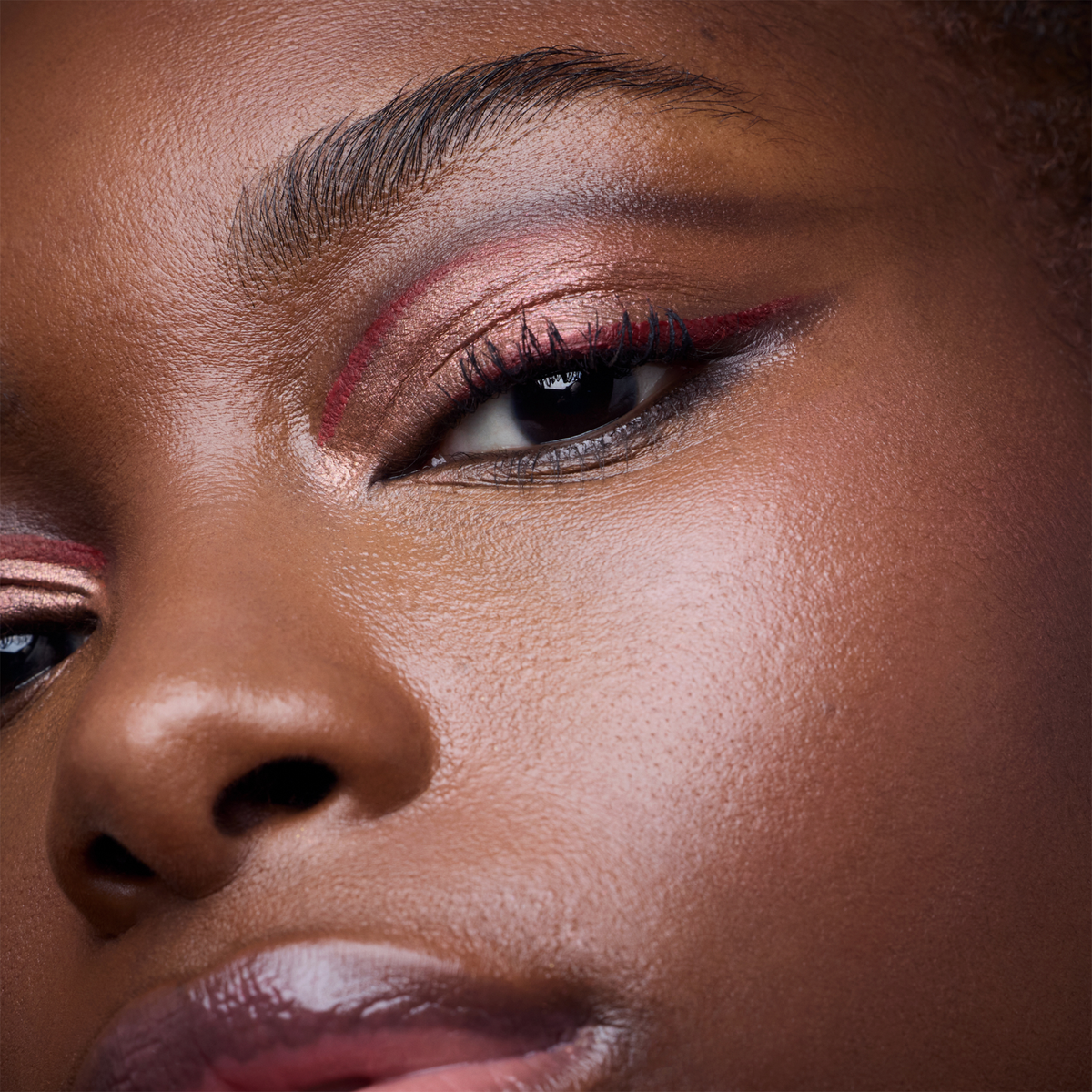 Nahaufnahme einer Person mit leuchtendem, schimmerndem Augen-Make-up in Rosa- und Rottönen aus der Wonder Woman-Lidschattenpalette.