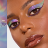 Nahaufnahme einer Person mit glänzenden Lippen und schimmerndem, mehrfarbigem, geflügeltem Lidschatten, akzentuiert durch lila Eyeliner, der mit dem Infinite Chrome Pencil von Danessa Myricks Beauty aufgetragen wurde.