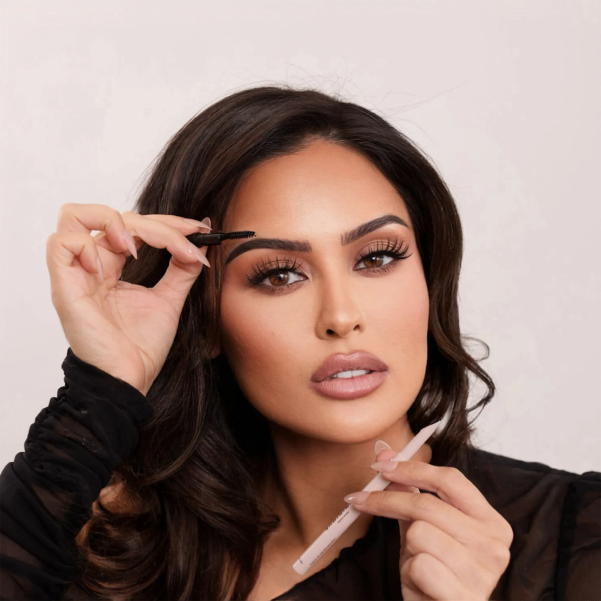 Frau mit perfekt gestylten Augenbrauen hält den Brow Frame Pencil Spoolie an die Braue und den Augenbrauenstift in der anderen Hand.