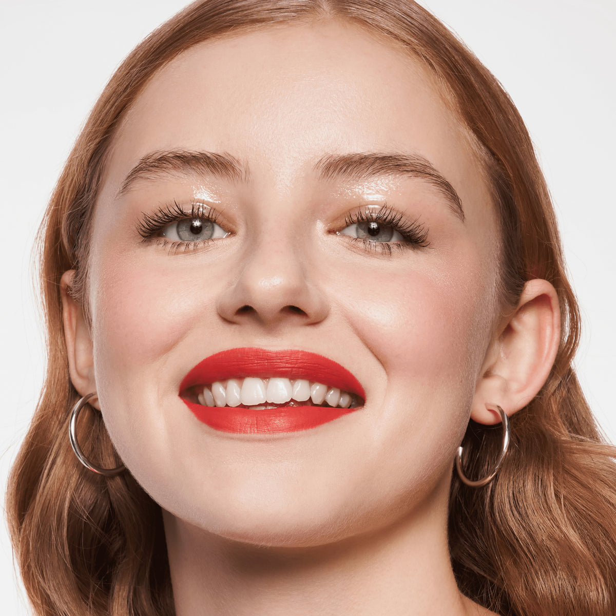 Lächelnde Frau mit hellem Hautton, rotem Lippenstift und hellbraunem Haar präsentiert ihren strahlenden Look mit MAGIC FILTER Glow Booster 10 Light.