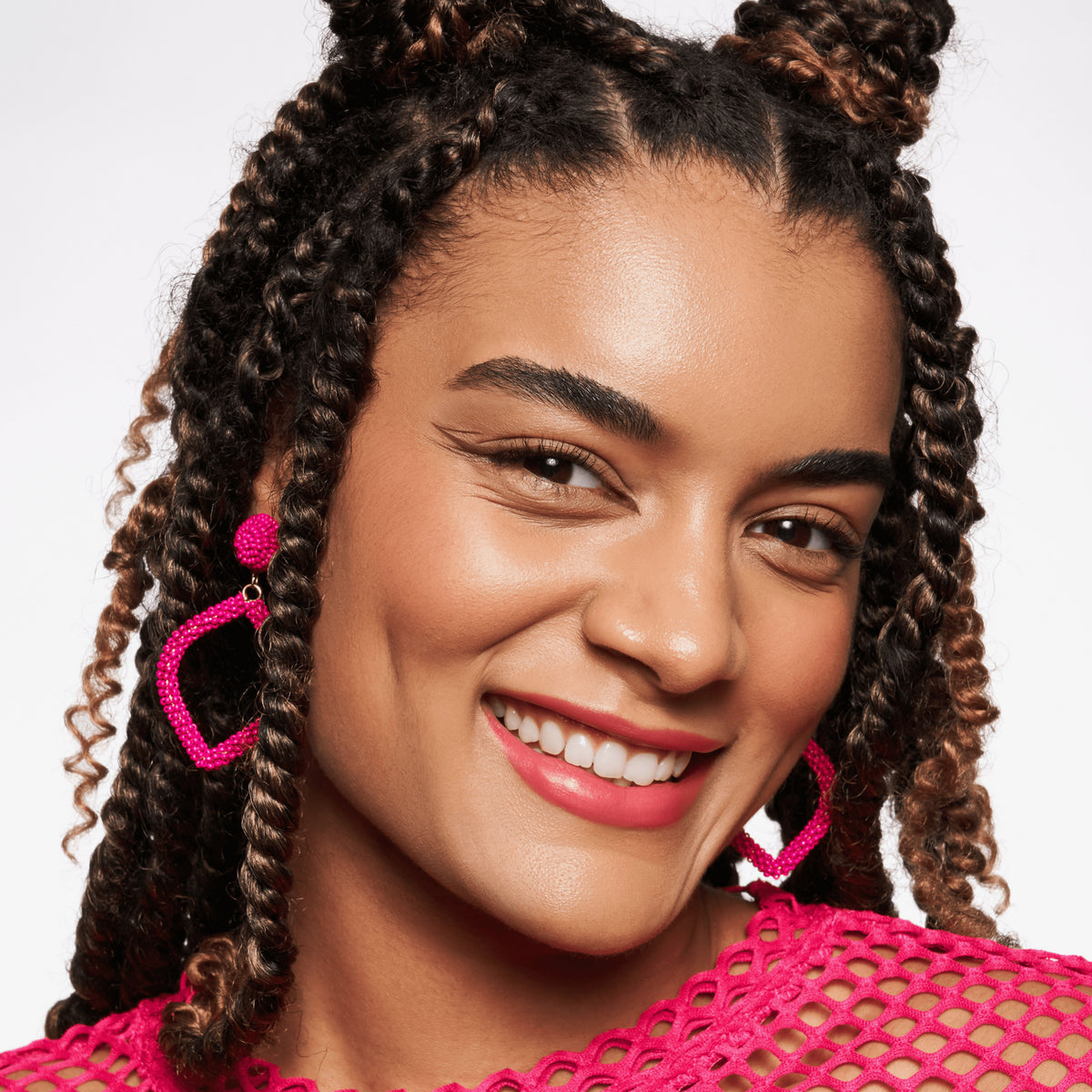 Lächelnde Frau mit mittlerem Hautton, rosarotem Lippenstift und dunkelbraunen Braids präsentiert ihren strahlenden Look mit MAGIC FILTER Glow Booster 30 Medium/ Tan.