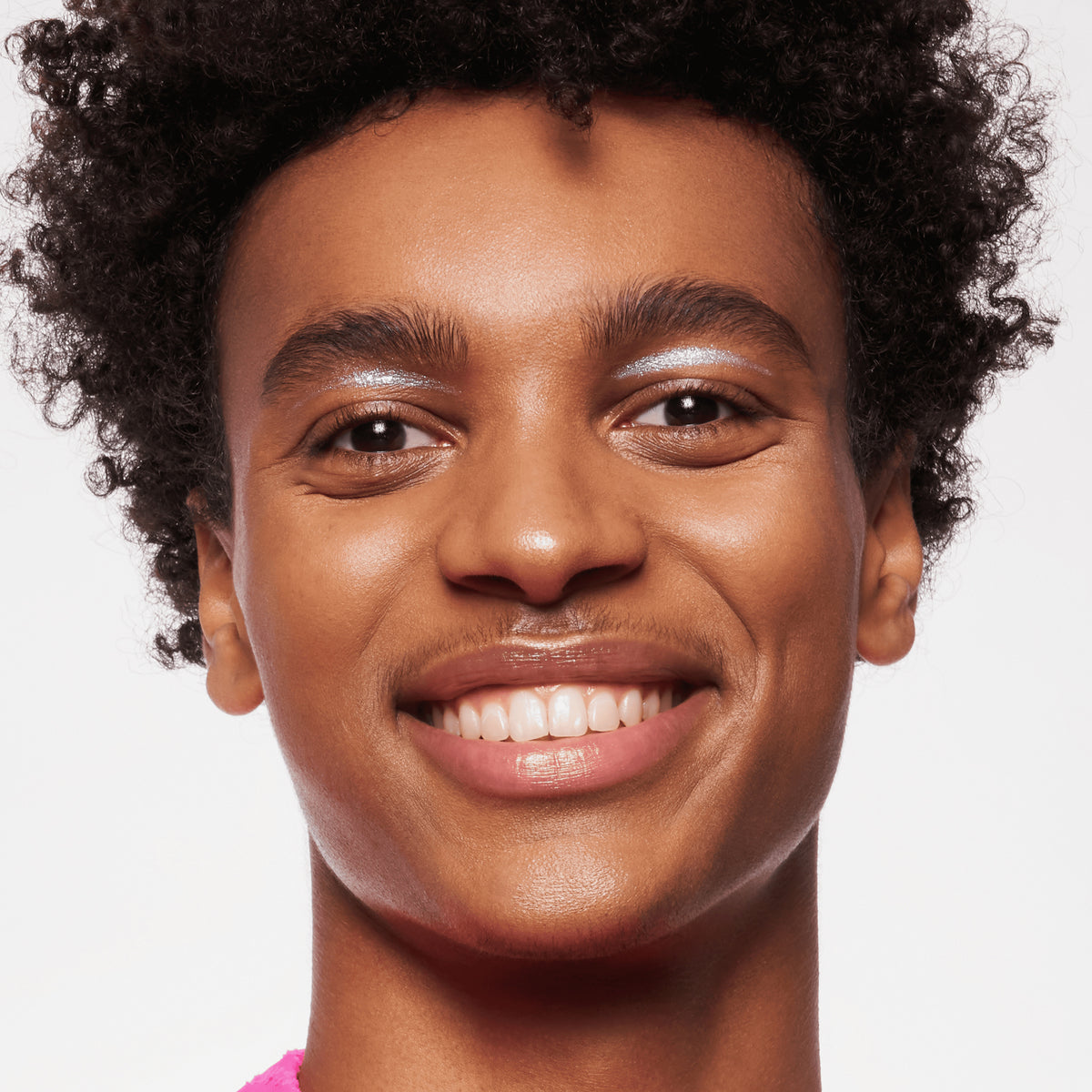 Person mit mittlerem bis dunklem Hautton, und dunkelbraunen Locken präsentiert ihren strahlenden Look mit MAGIC FILTER Glow Booster 50 Tan/ Deep.