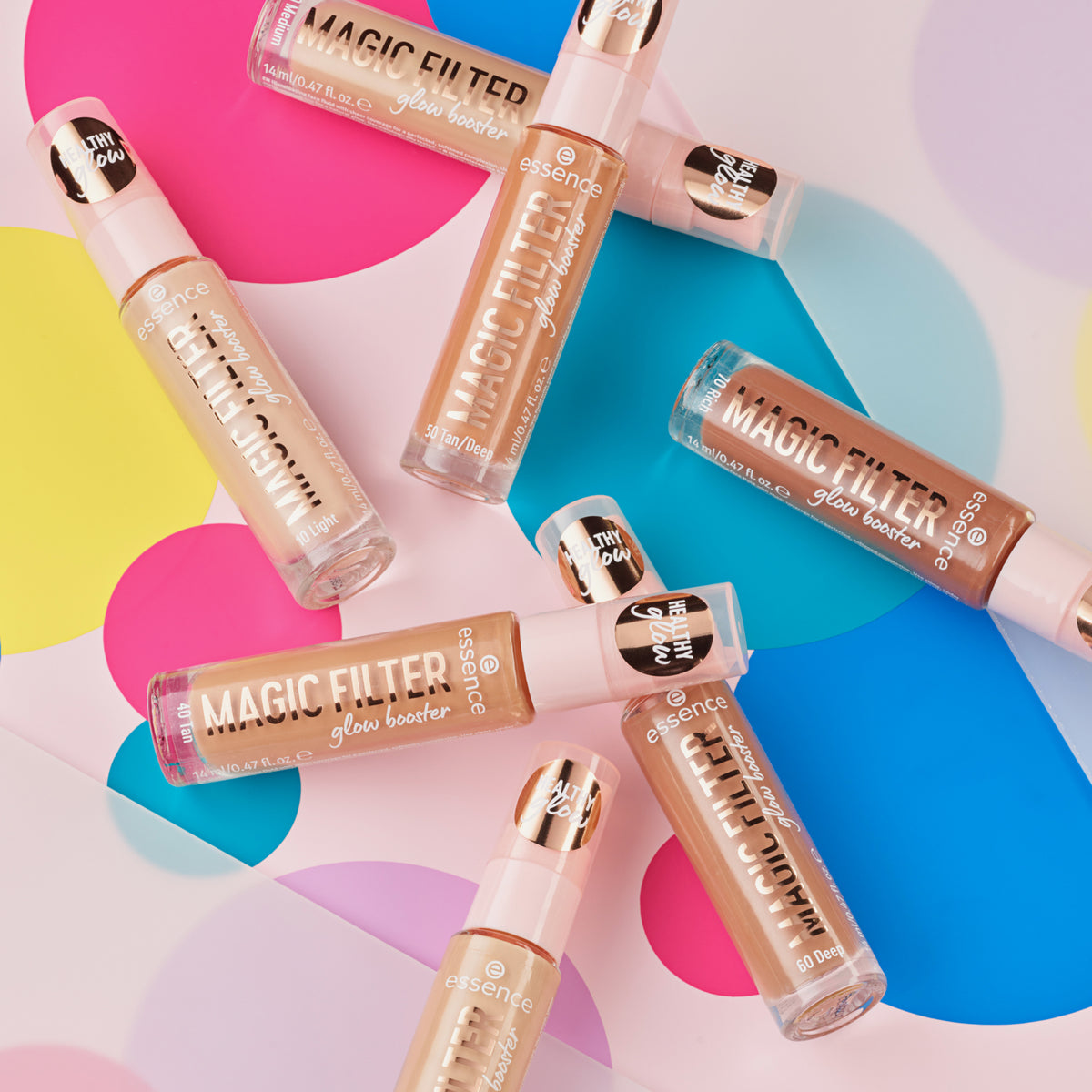 Mehrere Flaschen MAGIC FILTER Glow Booster liegen auf einem bunten geometrischen Hintergrund.