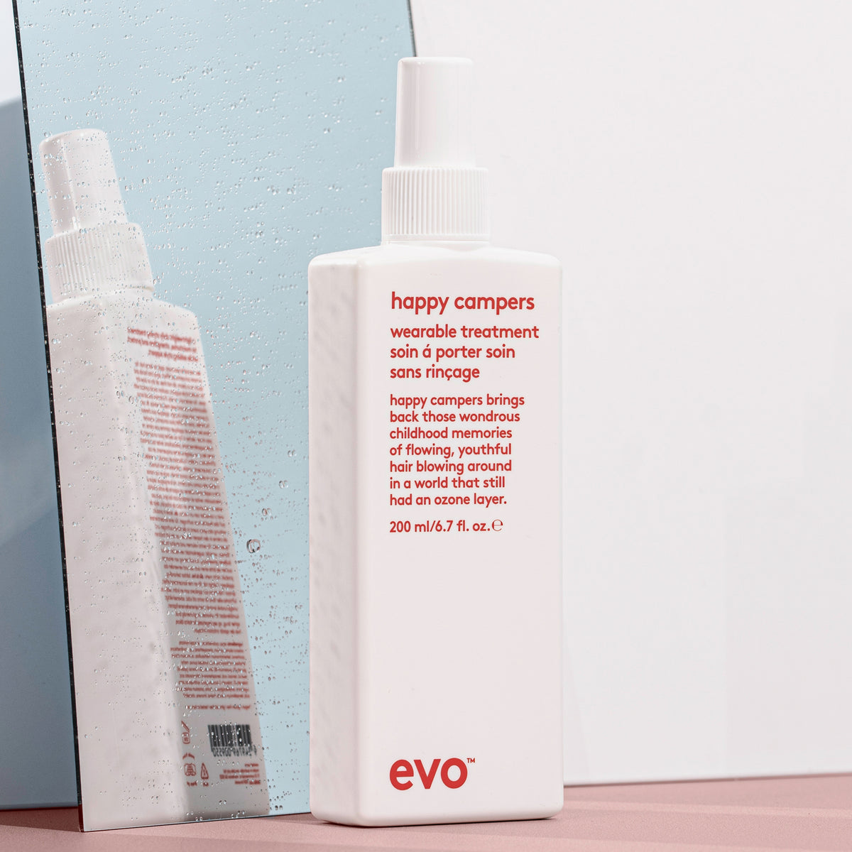 Eine Flasche Happy Campers Wearable Treatment vor einem nassen Spiegel.