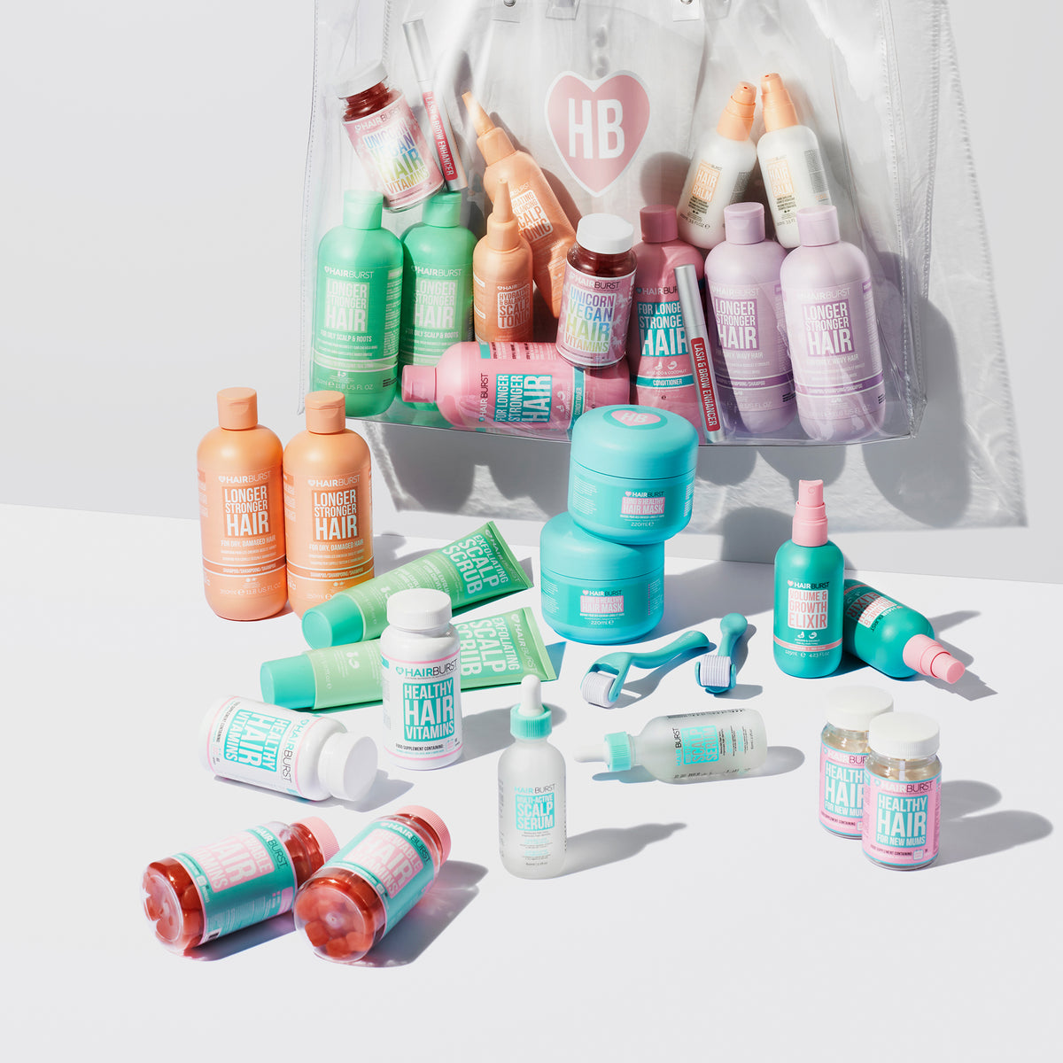 Farbenfrohe Hairburst-Produkte auf weißer Oberfläche, im Hintergrund ist eine durchsichtige Tasche mit dem HB-Logo zu sehen.