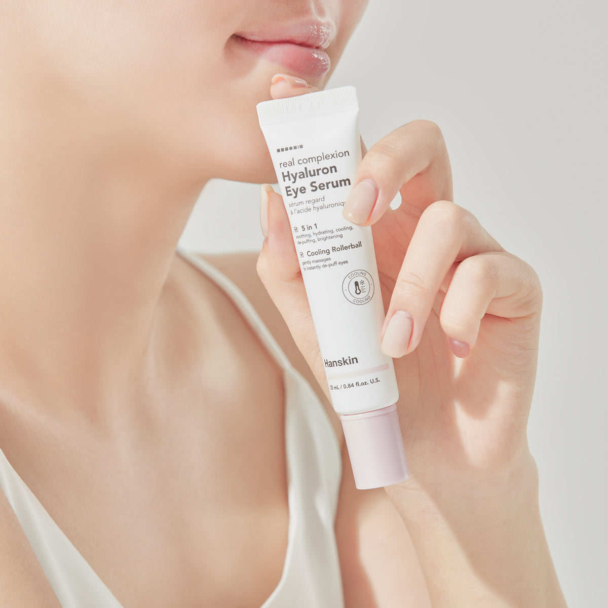 Frau hält vor einem hellen Hintergrund eine Tube Real Complexion Hyaluron Eye Serum vor ihr Gesicht.