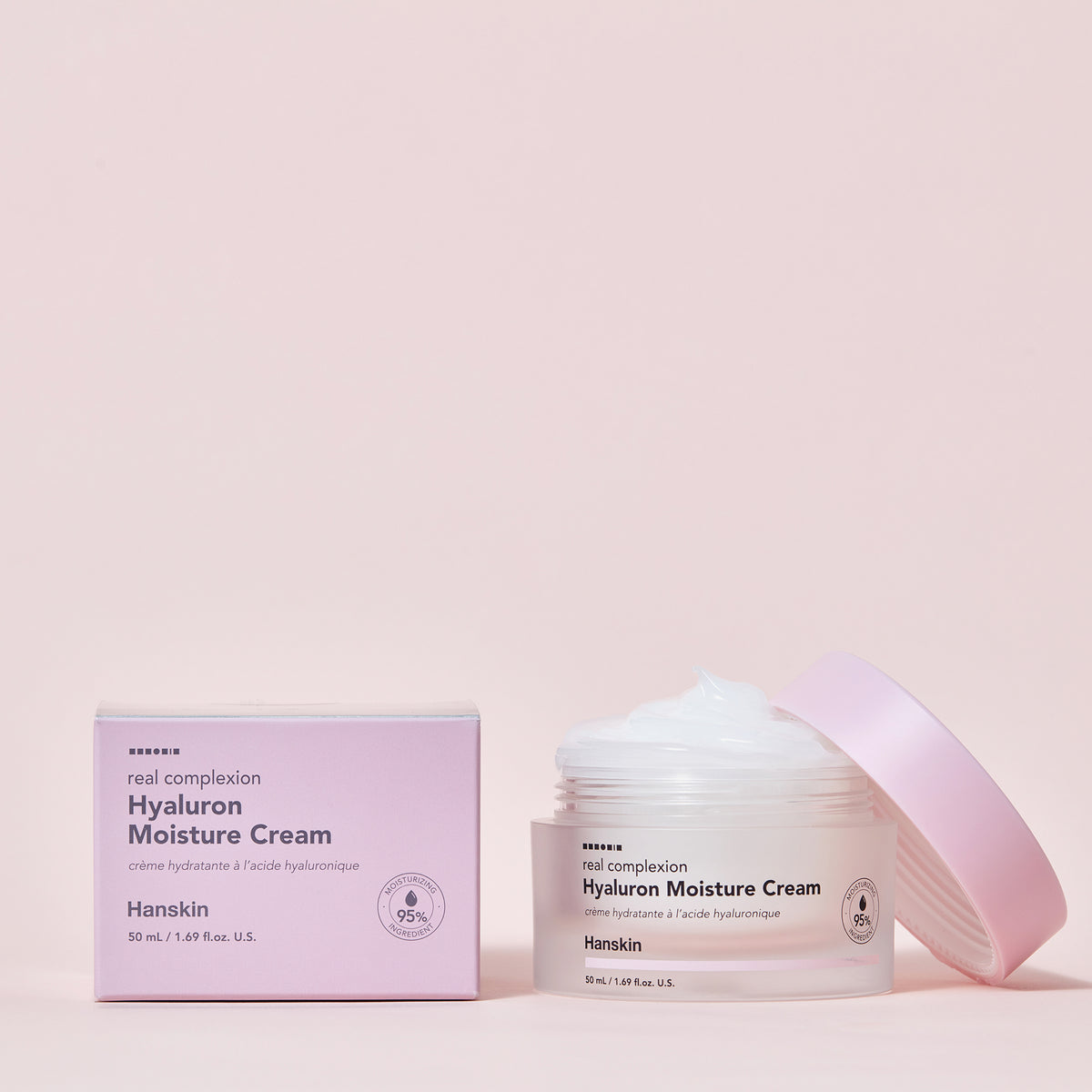Schachtel und offener Tiegel Hanskin Real Complexion Hyaluron Moisture Cream vor einem hellrosa Hintergrund.