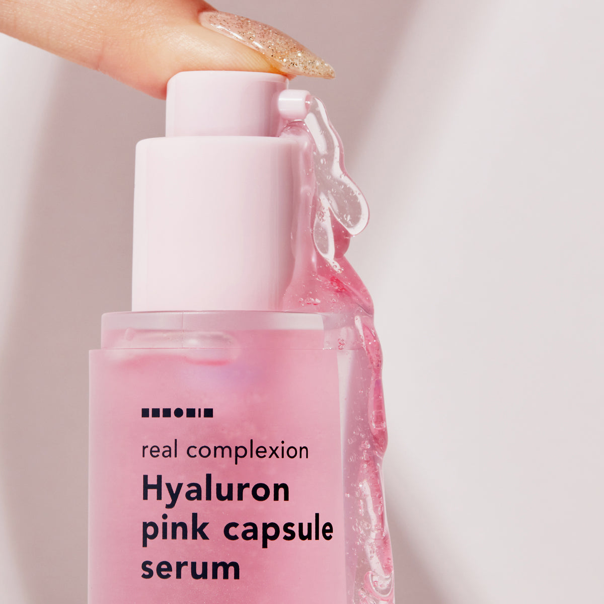 Eine Hand drückt die Real Complexion Hyaluron Pink Capsule Serum aus der rosa Flasche.