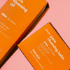 Zwei orangefarbene Hanskin-Boxen mit der Aufschrift „Pore Cleansing Oil AHA“ und „Pore Cleansing Balm AHA“ auf rosa Hintergrund.