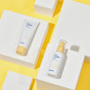 Das Hanskin Seven Layer Ceramide Serum und die Cream auf weißen Blöcken vor gelbem Hintergrund.