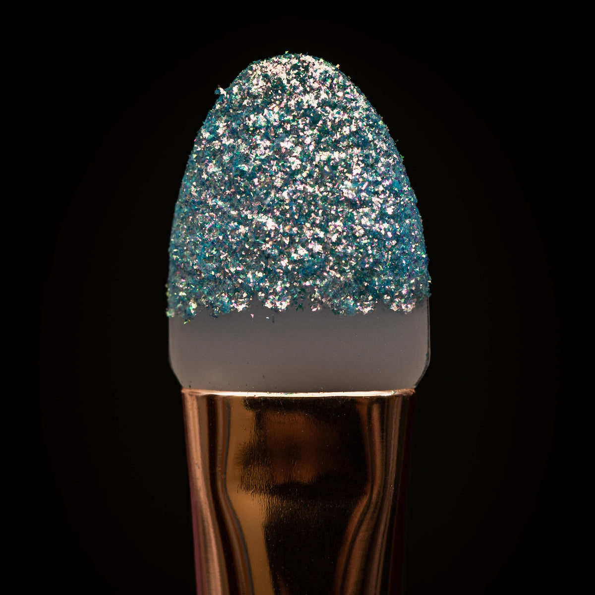 Nahaufnahme der Silikonspitze des K1: Eye & Lip Glitter Pigment Brush mit blau-silbernem Glitzer auf schwarzem Hintergrund.