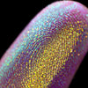 Nahaufnahme einer Fingerspitze, die in den Opal Moonstone Loose Multichrome Eyeshadow Cry Baby getaucht wurde und blau-violett und gelb glitzert.