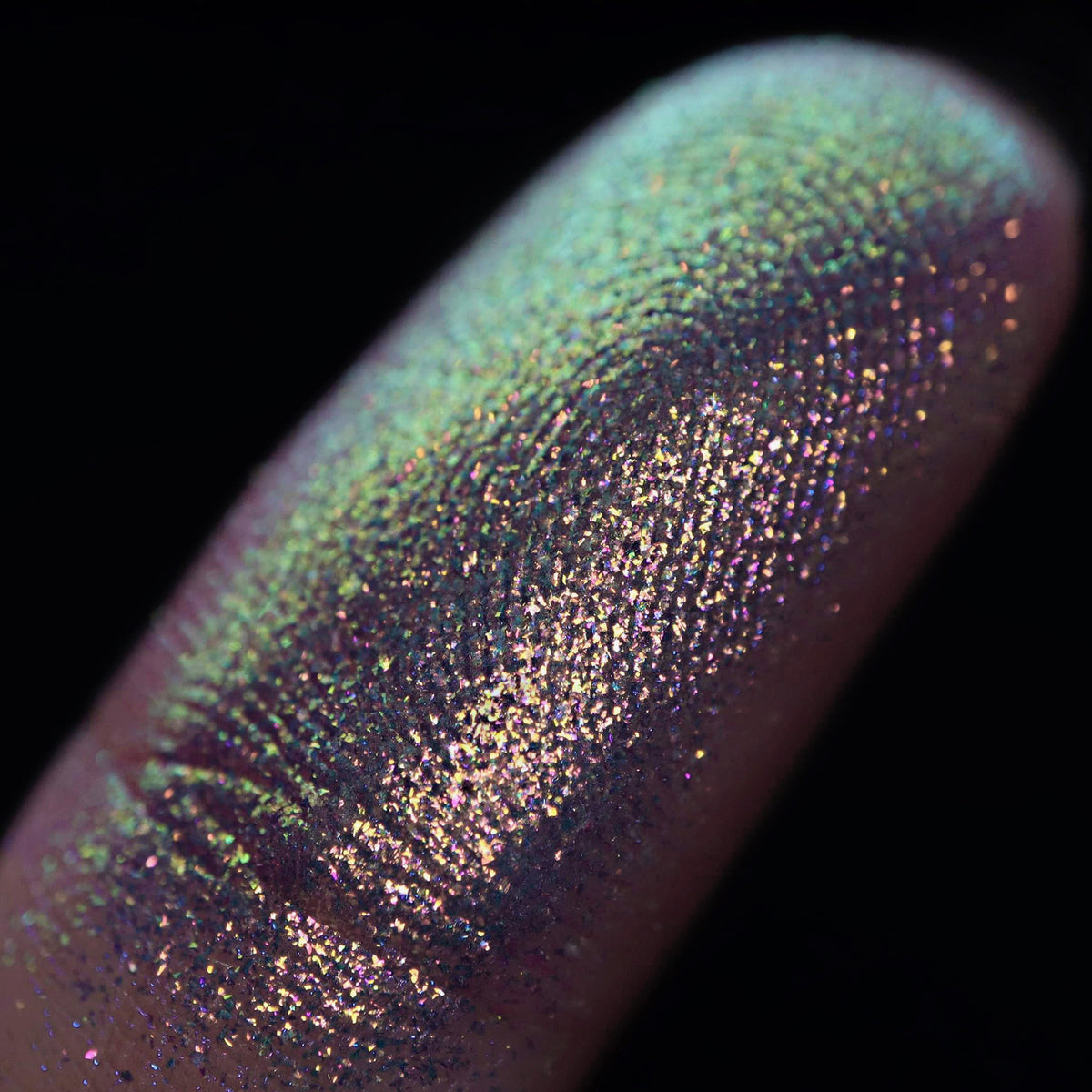 Nahaufnahme einer Fingerspitze, die in den Opal Multichrome Loose Eyeshadow Beauty Sleep getaucht wurde und grün und lila glitzert.