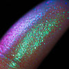 Nahaufnahme einer Fingerspitze, die in den Opal Multichrome Loose Eyeshadow Chill getaucht wurde und pink-lila und grün glitzert.