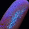 Nahaufnahme einer Fingerspitze, die in den Opal Multichrome Loose Eyeshadow Insomnia getaucht wurde und lila-blau glitzert.