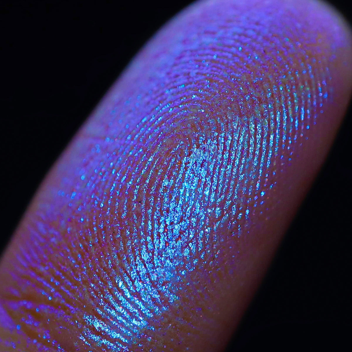 Nahaufnahme einer Fingerspitze, die in den Opal Multichrome Loose Eyeshadow Insomnia getaucht wurde und lila-blau glitzert.