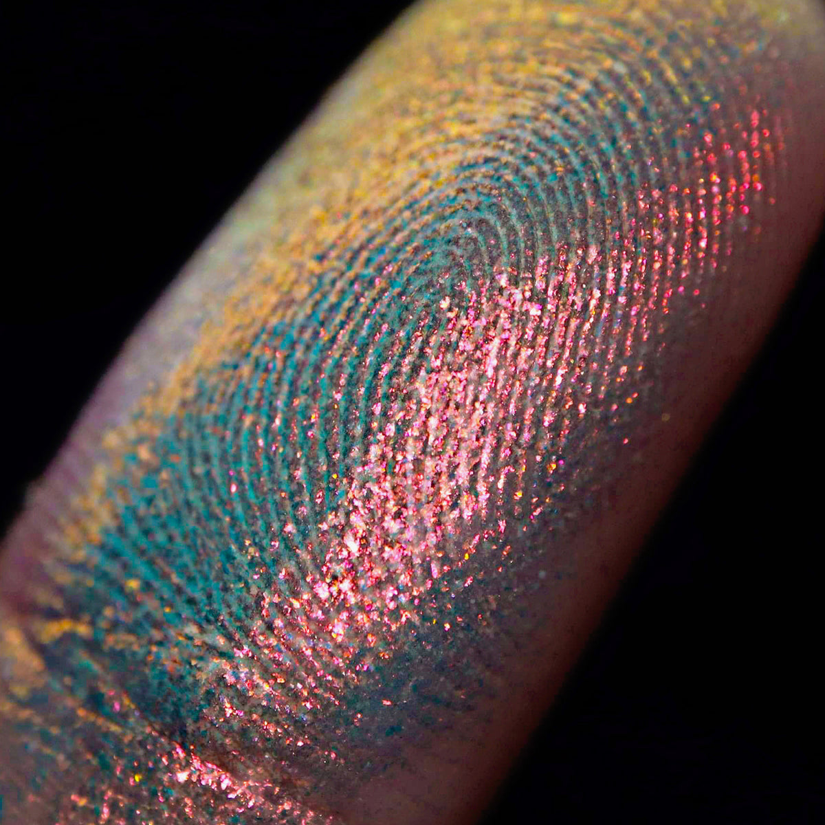 Nahaufnahme einer Fingerspitze, die in den Opal Multichrome Loose Eyeshadow Pillow Fight getaucht wurde und gelb-blau und rosa-bronze glitzert.