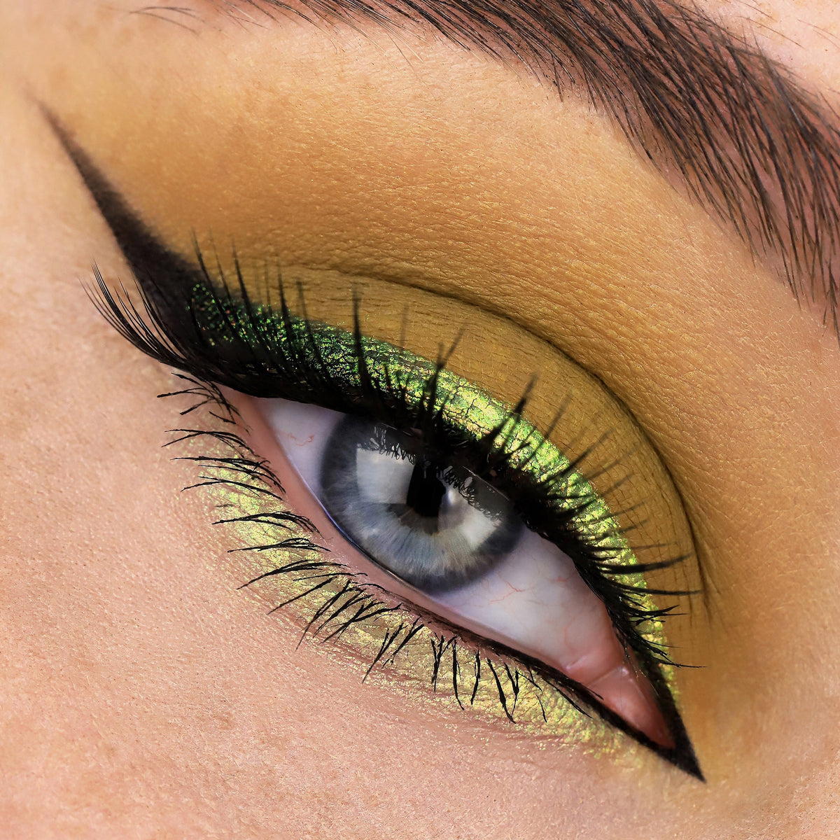 Nahaufnahme eines Auges mit dramatischem Eyeliner und gelb-grünlich schimmerndem Opal Multichrome Loose Eyeshadow in Teddy Bear.