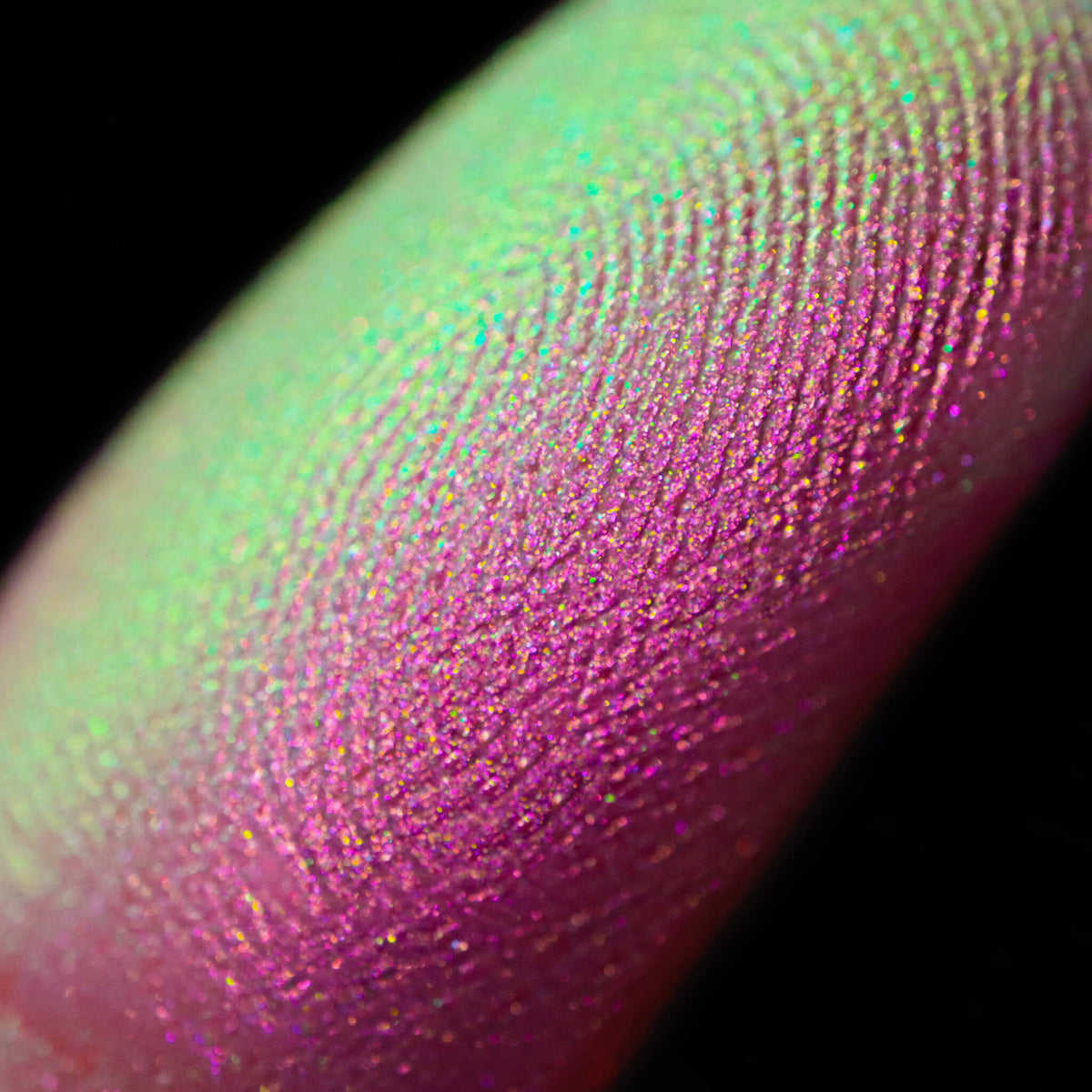 Nahaufnahme einer Fingerspitze, die in den Pastel Duochromes Loose Eyeshadow Cupcake getaucht wurde und hellgrün und pink glitzert.