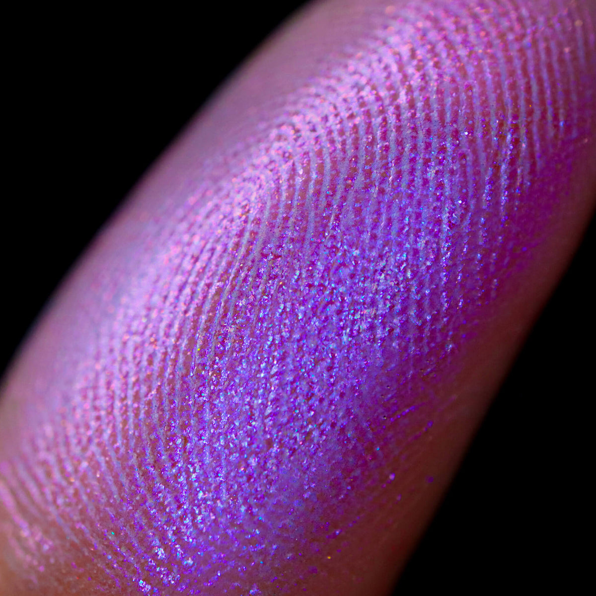 Nahaufnahme einer Fingerspitze, die in den Pastel Duochromes Loose Eyeshadow Frosting getaucht wurde und lila und pink glitzert.