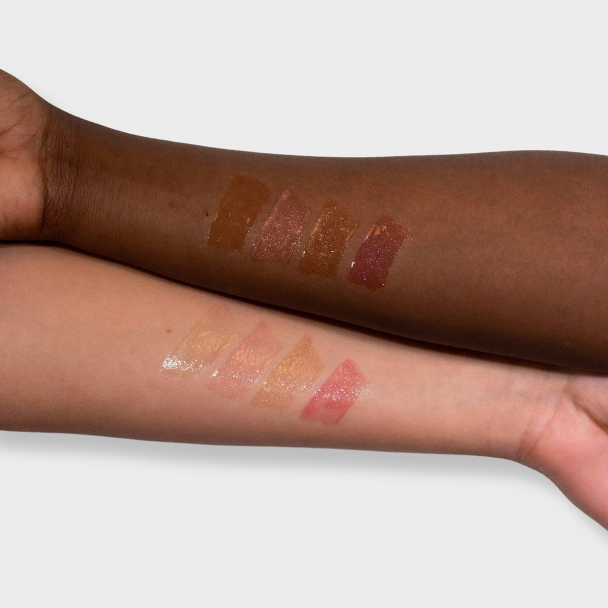 Zwei Arme mit unterschiedlichen Hauttönen zeigen drei glänzende und glitzernde Farbmuster des Glazed Lipgloss von LH Cosmetics.