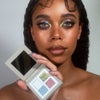 Eine Frau mit kräftigem, glitzerndem Lidschatten hält die Siren Song Palette von LH Cosmetics mit vier schimmernden Lidschattentönen.